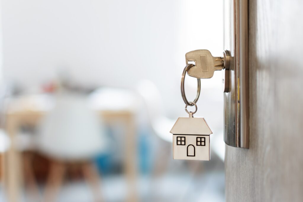 House key in a door with a home-shaped keychain, symbolizing buying a home.